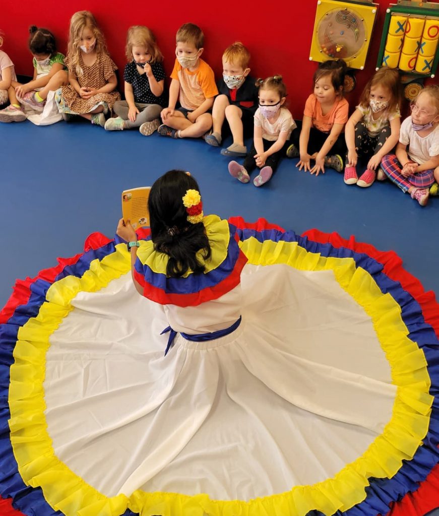 Children enjoying story time at a spanish immersion daycare program with an instruction dressed in traditional cultural clothing.