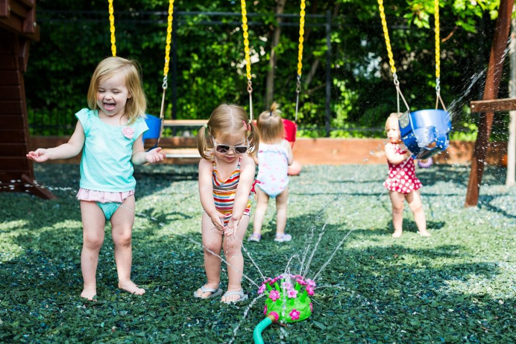 Toddlers engaging in play-based learning by splashing in in sprinkler